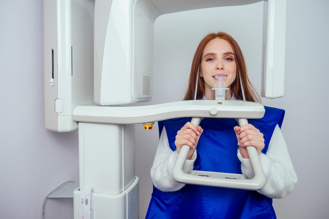 Close up head shot of redhaired ginger girl taking dental tac with cephalometric panorama xray machine in clinic